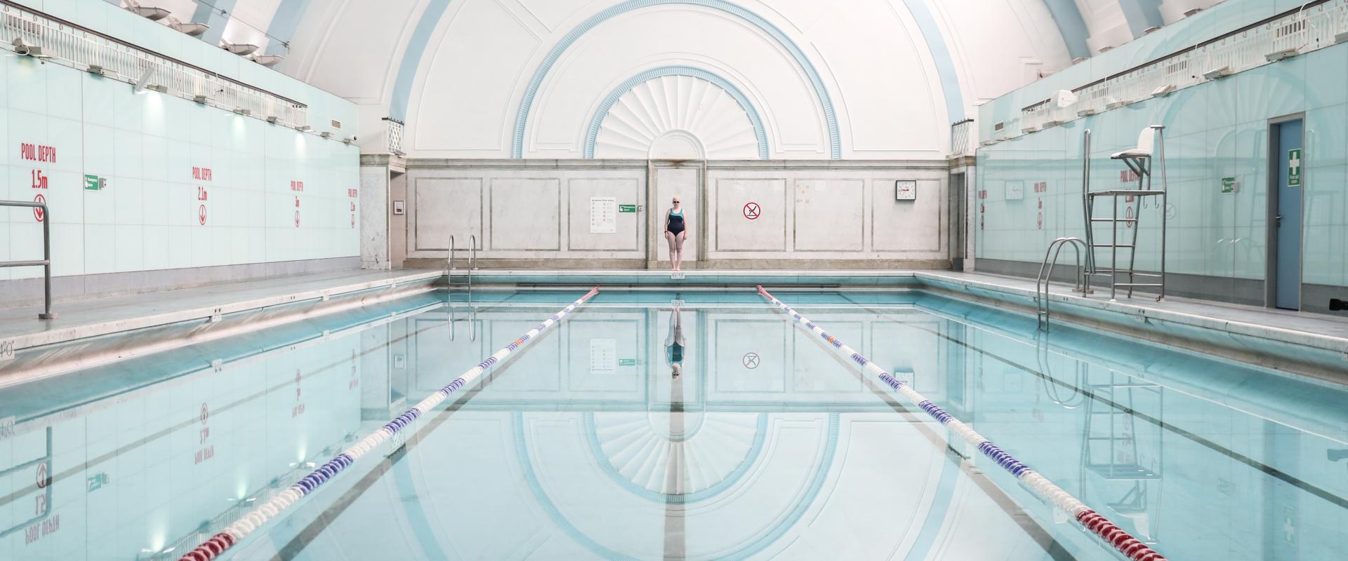 A woman standing at the far end of a swimming pool facing the camera